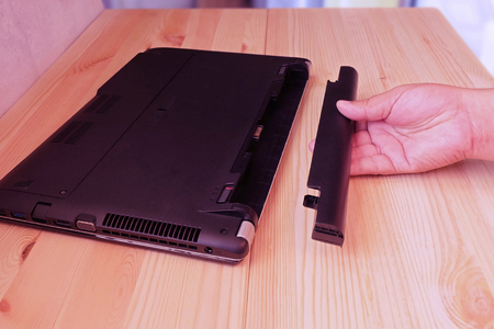Hand holding battery Remove of laptop computer on wooden floor, Upgrade and Repair computer concept.の写真素材