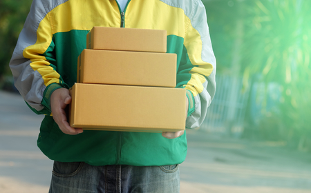 Delivery man staff in the colorful jacket uniform holds parcel box that is about to be delivered to customer with blurred background, with copy spaceの写真素材