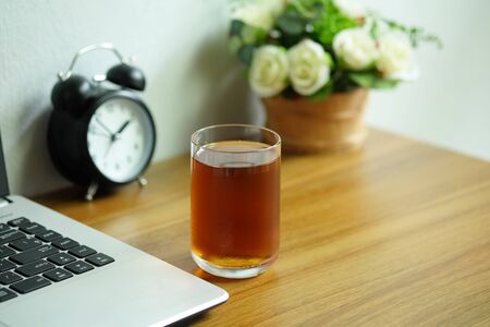 Tea in a clear glass on a wooden office desk with laptop computer, Tea afternoon break.の写真素材