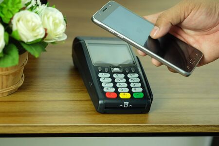 Hand of business man is holding smartphone and POS Terminal Credit Card Machine, wireless payment.