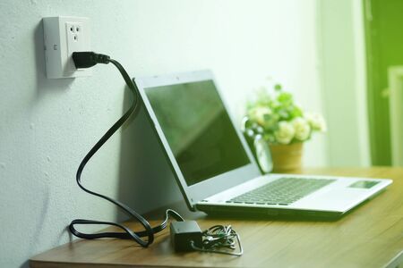 Plug in power outlet adapter cord charger on a white wall of the laptop computer on Wooden floor.の写真素材