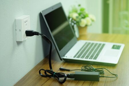 Plug in power outlet adapter cord charger on a white wall of the laptop computer on Wooden floor.の写真素材
