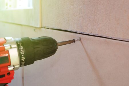Cordless drill screwing screw into a fiber cement board, Concept of construction or home maintenance and repair.の写真素材