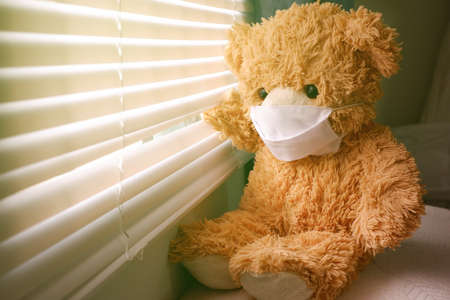 Teddy bear wearing a face mask, sitting and looking out the window with loneliness and Sadness. Coronavirus Covid-19 and pm2.5, stay at home, quarantine concept.の写真素材