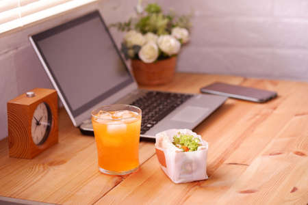 Eat sandwich and orange juice. During work with laptop computer. Work and eat food at the same time. Work at home.の写真素材