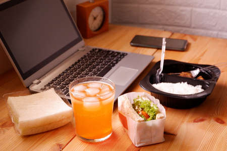 Eat sandwich and Meal plastic box with orange juice. During work with laptop computer. Work and eat food at the same time. Work at home.の写真素材