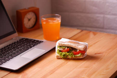 Eat sandwich and orange juice. During work with laptop computer. Work and eat food at the same time. Work at home.の写真素材