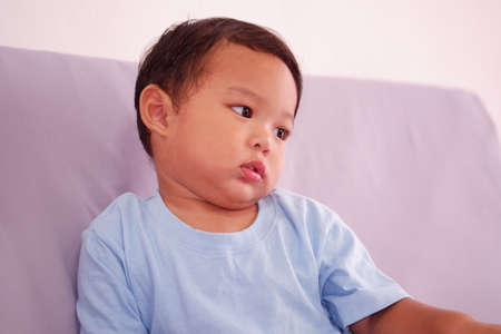 Asian boy about 2 years old with a cold, runny or sick nose, sits on the sofa in the living room.の写真素材