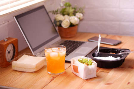 Eat sandwich and Meal plastic box with orange juice. During work with laptop computer. Work and eat food at the same time. Work at home.の写真素材