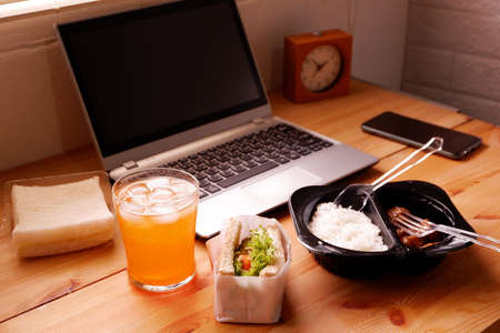 Eat sandwich and Meal plastic box with orange juice. During work with laptop computer. Work and eat food at the same time. Work at home.の写真素材