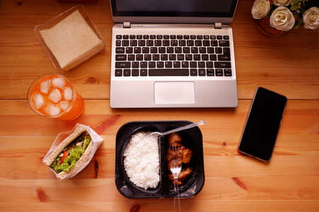 Eat sandwich and Meal plastic box with orange juice. During work with laptop computer. Work and eat food at the same time. Work at home.の写真素材