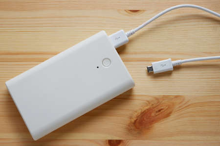 White power bank or backup battery with USB 2.0 cable charger on wooden background.Top view.
