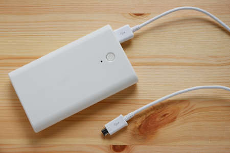 White power bank or backup battery with USB 2.0 cable charger on wooden background.Top view.の写真素材
