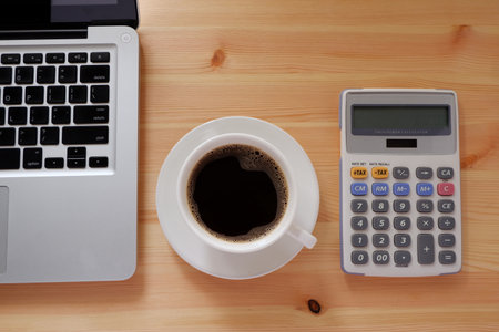 Laptop computer and calculator and black coffee in white cup on wooden desk with copy space, Top...
