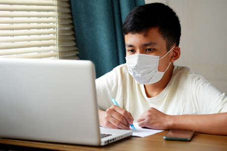 Asian boy wearing face mask and looked at laptop computer to study online, Online education via the internet during the   epidemic, stay at home, quarantine concept.の写真素材