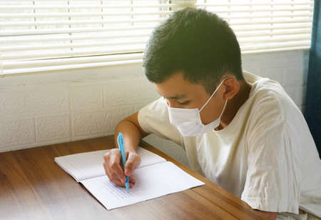 Asian boys cover their faces with masks and write or do homework during the outbreak at home.の写真素材