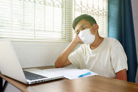 Asian boy wearing face mask and looked at laptop computer to study online, Bored with online education via the internet during the epidemic, stay at home, quarantine concept.の写真素材