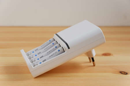 Rechargeable AAA battery in a white charger on wooden background.の写真素材