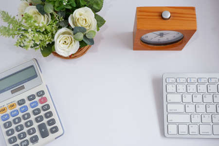 Computer keyboard with calculator and flowerpot on white desk, with copy space for text.の写真素材