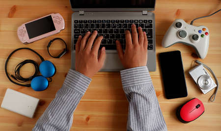 Businessman working from home with laptop computer and Smartphone with portable game consoles and many electronic gadgets devices on wooden desk. Top view.の写真素材