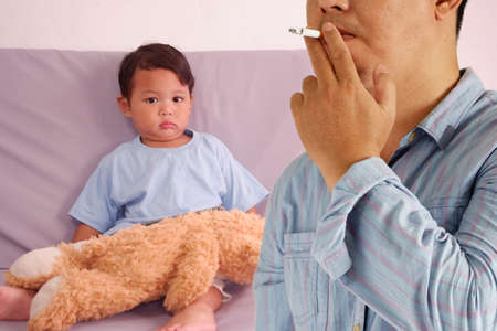 Man smoking cigarette and asian boys background, It is dangerous for people around.の写真素材