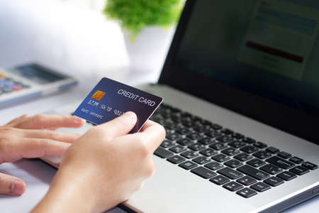 Female hand holding credit card and laptop computer on white desk. Concept of Online shopping and payment.の写真素材