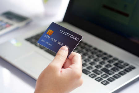 Female hand holding credit card and laptop computer on white desk. Concept of Online shopping and payment.の写真素材