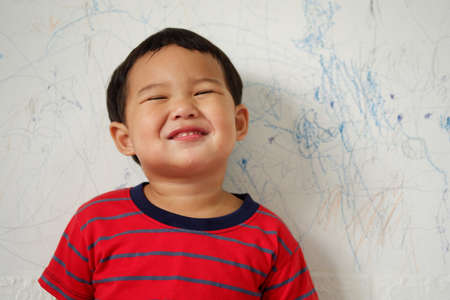Cute smiling Asian boy wearing a bright red striped T-shirt standing on white background. with text...