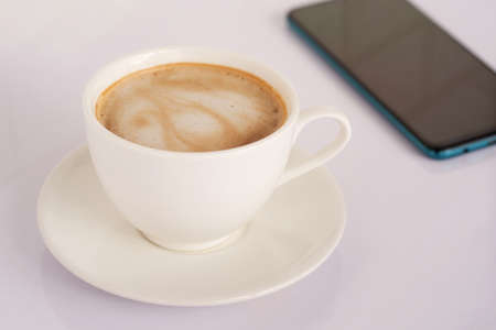 White latte coffee mug, side view on white desk and mobile phoneの写真素材