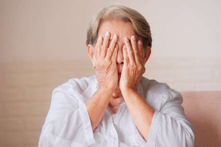 Elderly Asian woman with gray hair covering both eyes with hands, blindness, cataracts, pterygium, eye disease conceptの写真素材