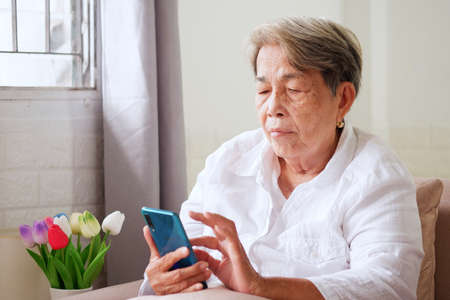 Elderly Asian woman with grey hair using mobile phone with indifferent or sad expression. Aging society Sad and lonely concept, with copy space for text.の写真素材