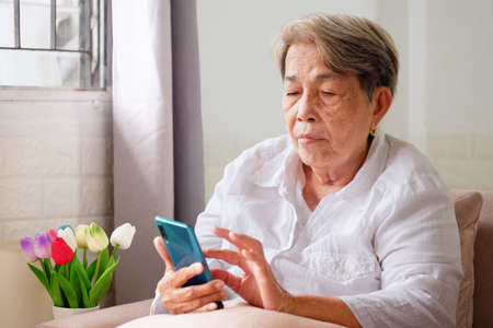 Elderly Asian woman with grey hair using mobile phone with indifferent or sad expression. Aging society Sad and lonely concept, with copy space for text.の写真素材