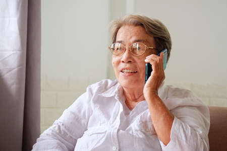 Elderly Asian woman with grey hair is using mobile phone with a happy smile. Aging society Sad and lonely concept, with copy space for text.の写真素材