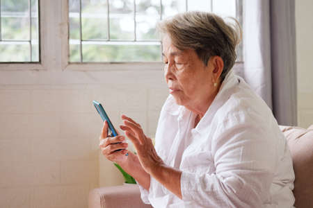 Elderly Asian woman with grey hair using mobile phone with indifferent or sad expression. Aging society Sad and lonely concept, with copy space for text.の写真素材