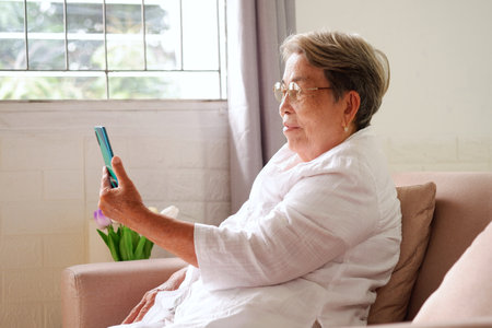 Elderly Asian woman with grey hair is using mobile phone with a happy smile. Aging society Sad and lonely concept, with copy space for text.の写真素材