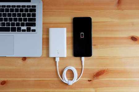 Plug in USB charger from powerbank input mobile phone or smartphone and laptop computer on wooden floor, Top view.の写真素材