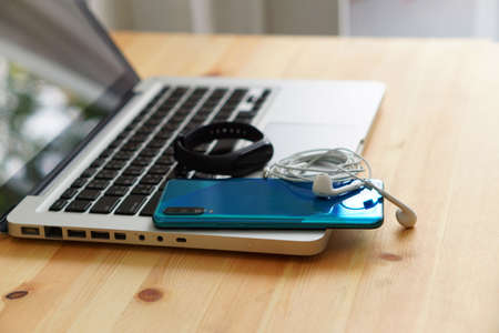 Smartphone and earphones and smart watch on the laptop computer, electronic gadgets for daily use on wooden background.の写真素材