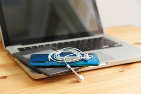 Smartphone and e-books, tablet and earphones on the laptop computer, electronic gadgets for daily use on wooden background.の写真素材