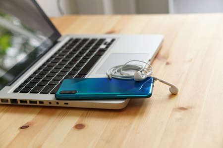 Smartphone and earphones on the laptop computer, electronic gadgets for daily use on wooden background.の写真素材