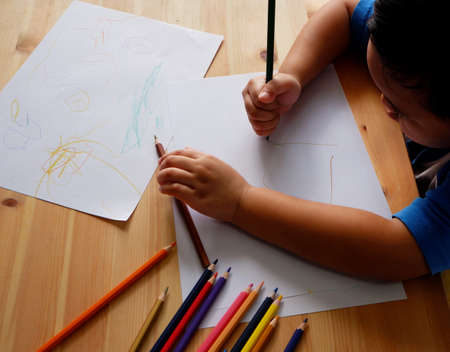 Cute Asian boy drawing with color pencils and white paper on wooden tableの写真素材