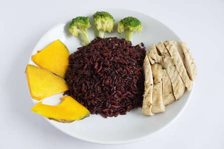 Close-up of riceberry cooked and chicken breast with Boiled broccoli and pumpkin on a white plate on a white background Healthy, clean organic food, rich in antioxidants and high in fiberの写真素材