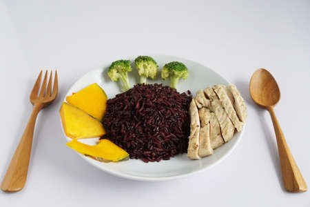 Close-up of riceberry cooked and chicken breast with Boiled broccoli and pumpkin on a white plate on a white background Healthy, clean organic food, rich in antioxidants and high in fiberの写真素材