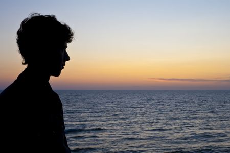 Silhouette of a young man looking off into the sunsetの写真素材