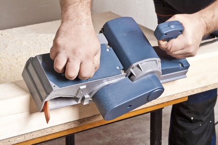 Close-up of a construction worker's hand and power tool while planing a piece of wood trim for a...