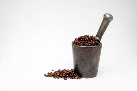black coffee grains in a metal authentic mortar with a handful of black coffee beans lying next to itの写真素材