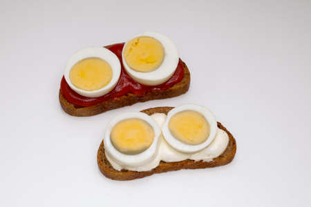 Two sandwiches. One of rye bread, with tomato sauce and two pieces of boiled egg on a white background, the second sandwich with white sauceの写真素材