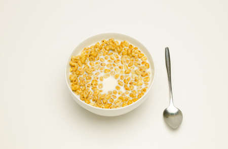 Wheat flakes with milk in a white cup and spoon on a white backgroundの写真素材