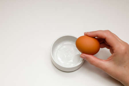 A woman's hand breaking a raw chicken egg into a white cup on a white backgroundの写真素材