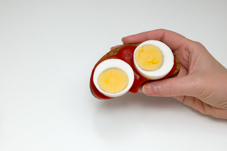Female hand with rye bread sandwich, tomato sauce and two pieces of boiled egg on a white backgroundの写真素材