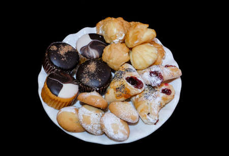 cookies, capcakes and other sweets in a white plate on a black backgroundの写真素材